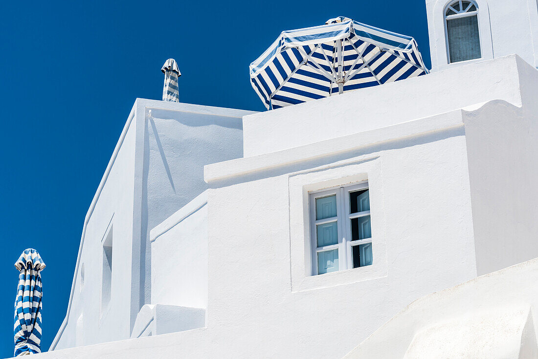 Eines der typischen Wohnhäuser am Steilhang mit Sonnenschirmen in den dominierenden Farben der Insel blau weiß, Imerovigli, Santorin, Kykladen, Griechenland