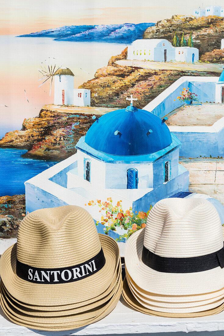 Stall for Santorini hats for tourists in front of a painting of the island, Firostefani, Santorin,  Cyclades, Greece