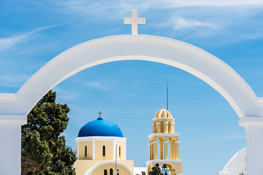 Blick durch einen Bogen mit Kreuz auf  Glockenturm und Kuppel der im traditionellen Stil erbauten Kirche von St. George Kirche, Ekklisia Agios Georgios, Oia, Kykladen, Santorini Griechenland