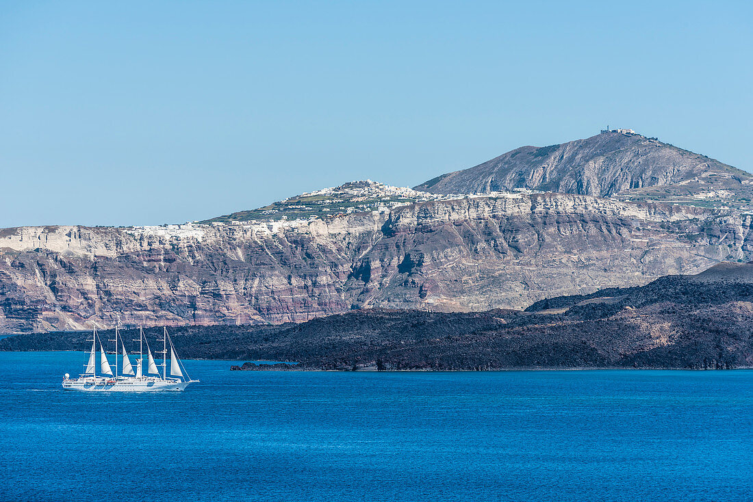 A sailing ship / cruise ship in front of the scenery of the island Santorin with the steep coast and the village Akrotiri in the background, Santorin, Cyclades, Greece