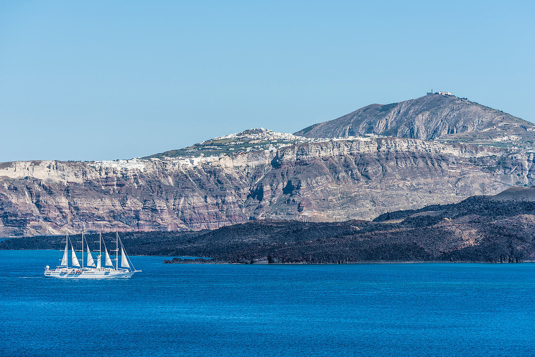 Ein Segelschiff / Kreuzfahrtschiff vor der Kulisse der Insel Santorin mit der Steilküste und dem Dorf Akrotiri im Hintergrund, Santorin, Kykladen, Griechenland