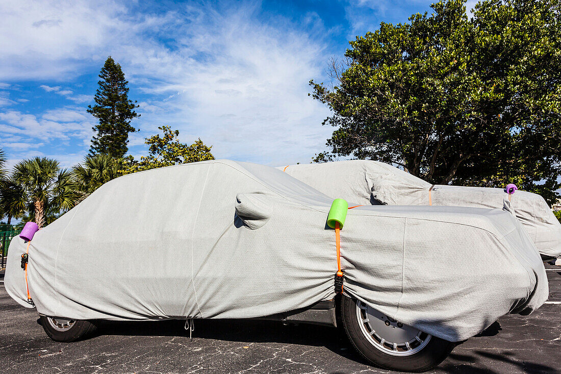 Autos auf einem Parkplatz die von den Besitzern zum Überwintern abgedeckt wurden, mit Palmen im Hintergrund, Sanibel, Florida, USA