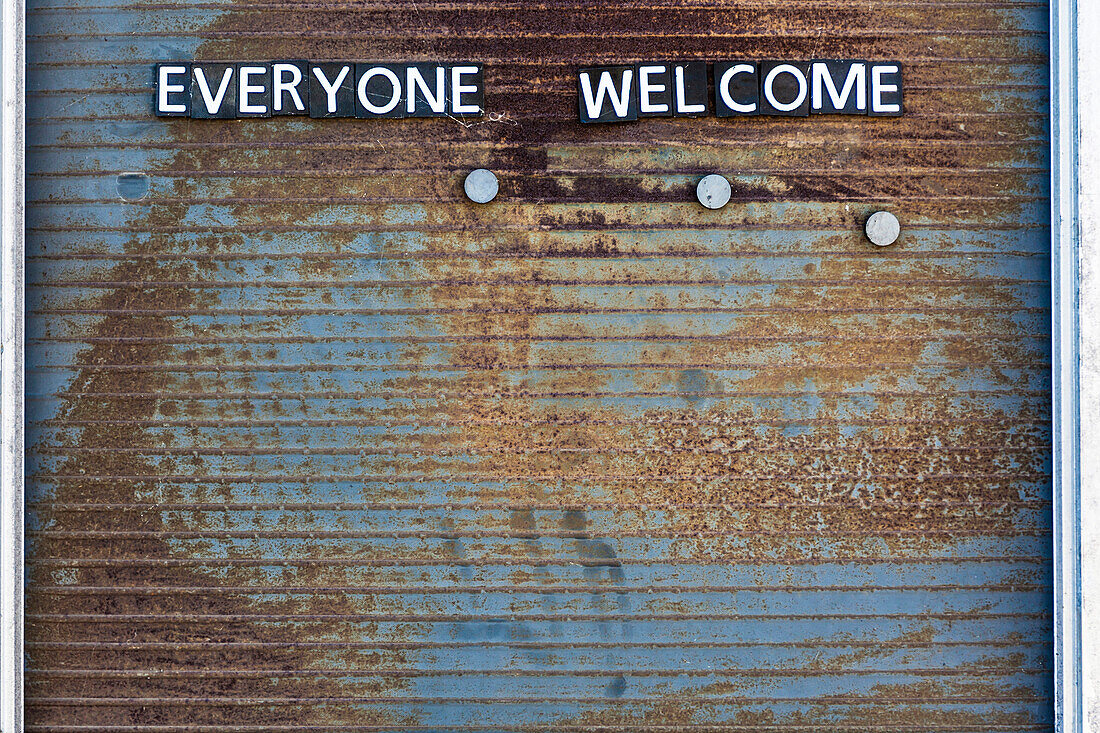 A weather-beaten information board with the stroke everyone welcome from single metal letters, Toronto, Canada