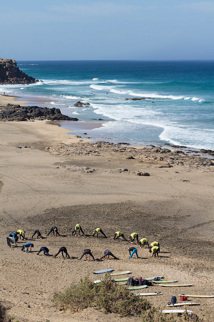 Group of surfers doing stretching in Cotillo beach in Fuerteventura, Canary Islands.