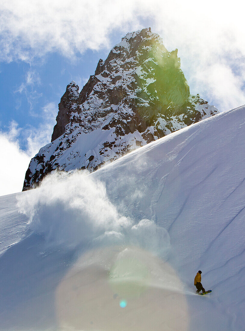 A man does a pow slash in the late sun light in the Whistler Backcountry and looks back at his trail.