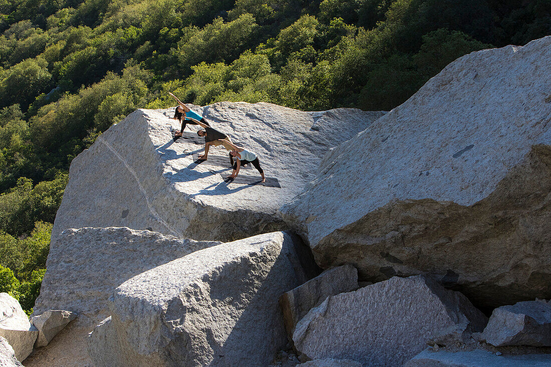 Three people do yoga on a rock platform in Little Cottonwood Canyon, Utah.