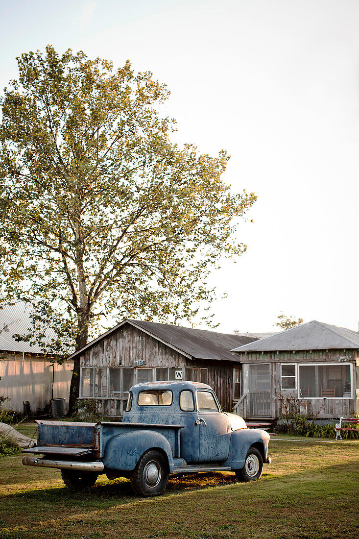 Rural scene with old truck and wooden cabin at sunset.