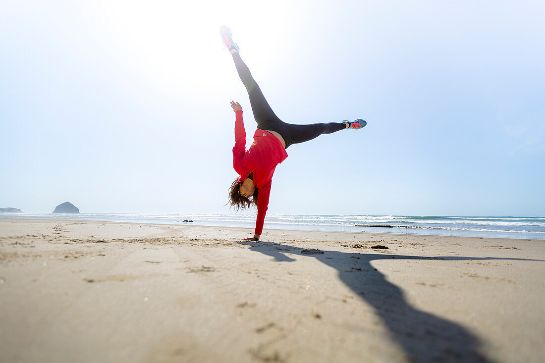 Girl does one handed cartwheel on the beach.