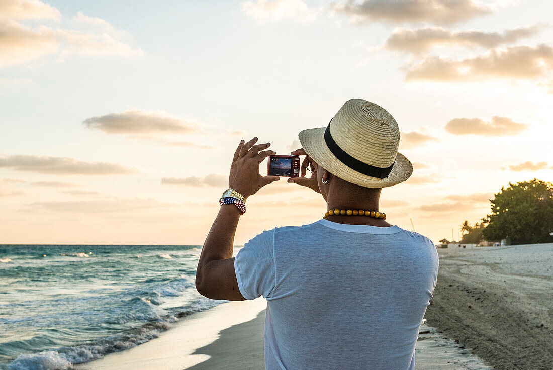 Back of Cuban man walking on Varadero Beach, taking vacation pictures at sunrise