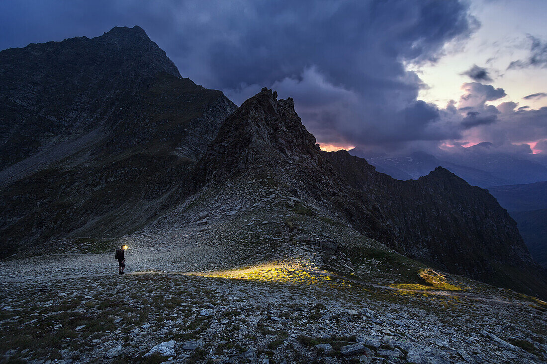 Hiker passes over the Gliederscharte mountain gorge at nightfall, Pfitsch, Part of the long distance hiking trail from Munich to Venice, South Tyrol, Italy