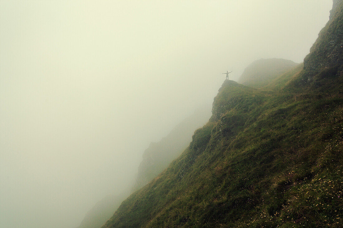 Hiker standing on a rock, surrounded by fog in the Pfunderer Mountains, South Tyrol, Italy