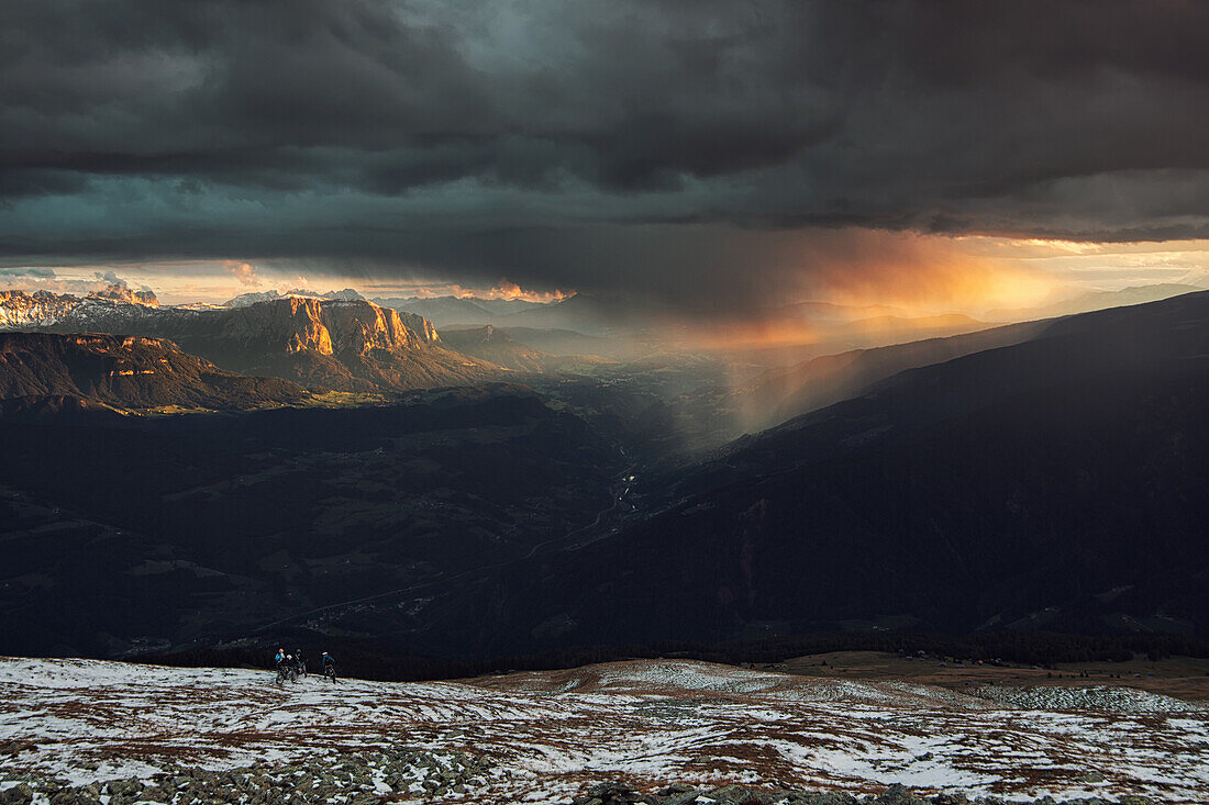 View from Koenigsangerspitze at sunset in the direction of Eisack Valley, On the left the Dolomites, Unesco world heritage, reflecting the last light of the day,  A group of motocross bikers watching the storm front pass through, South Tyrol, Italy