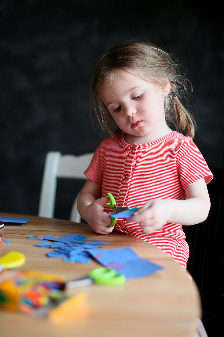 A four year old cutting paper and making crafts at home.
