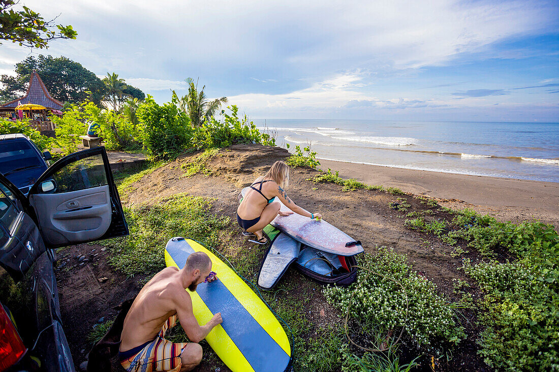 Young surfers are waxing their boards before surf session.