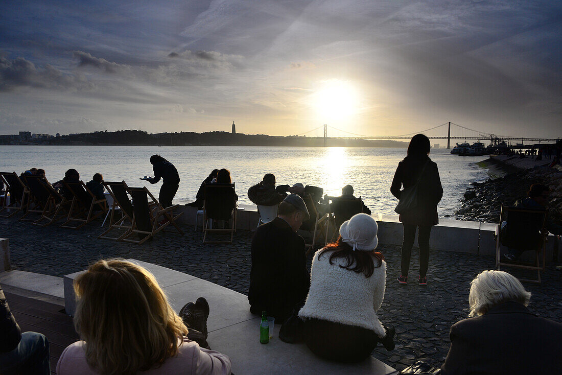 People sitting along the river Tejo at Cais do Sodre at sunset, Lisbon, Portugal