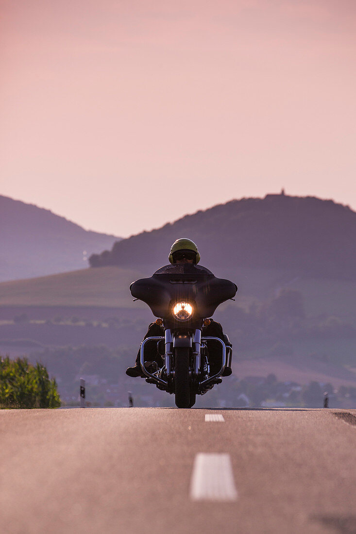 Man rides Harley-Davidson motorcycle on road to Point Alpha Memorial with Gehilfersberg mountain behind