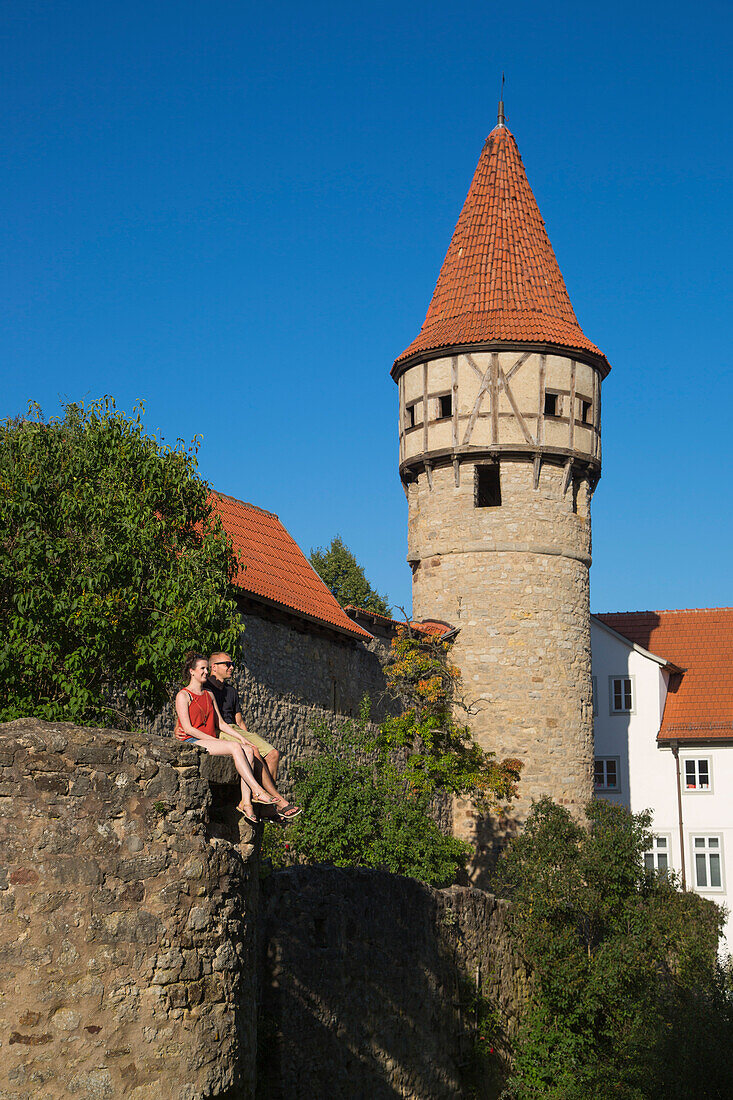 Junges Paar sitzt auf Mauer nahe Turm der Kirchenburg in der Altstadt, Ostheim, Rhön, Bayern, Deutschland