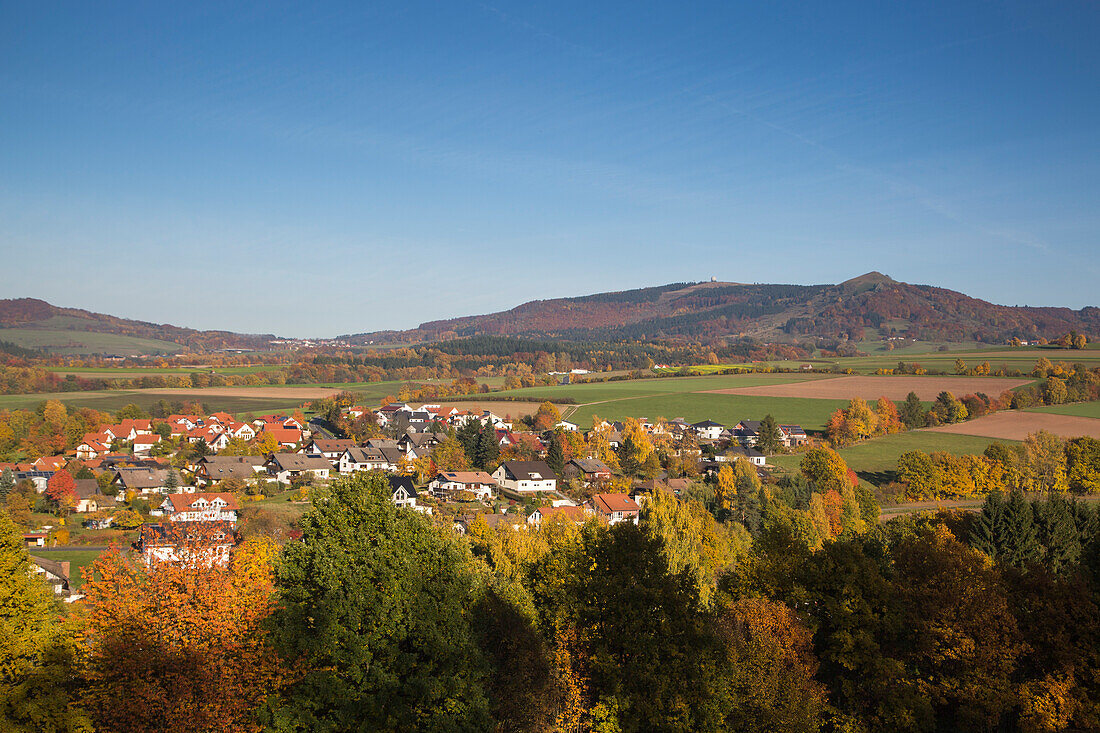 Blick auf Poppenhausen und Bäume mit buntem Herbstlaub mit der Wasserkuppe dahinter, Kleinsassen, Rhön, Hessen, Deutschland