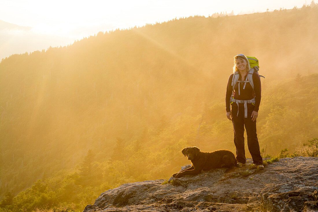 A woman and her dog watching the sunset on Grassy Ridge while backpacking on the Roan Highlands near  Bakersville, North Carolina.
