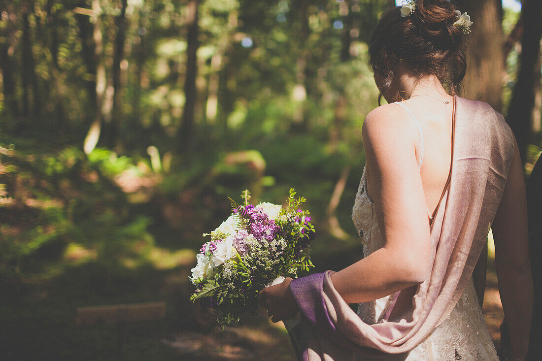 A young woman holds a bouquet of flowers in a forest setting.