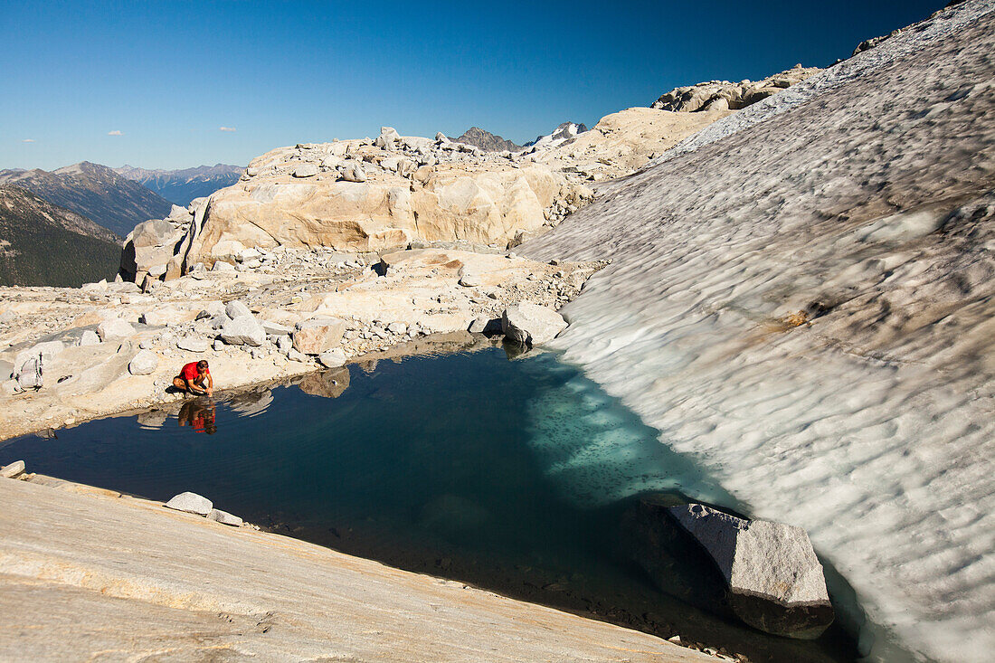 A hiker stops tos wash his hands in a glacier fed alpine tarn near Whistler, British Columbia, Canada.