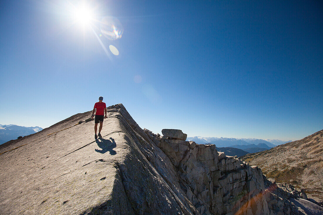 A hiker walks across a rocky slab ridge near the summit of Cassiope Peak, Pemberton, British Columbia, Canada.