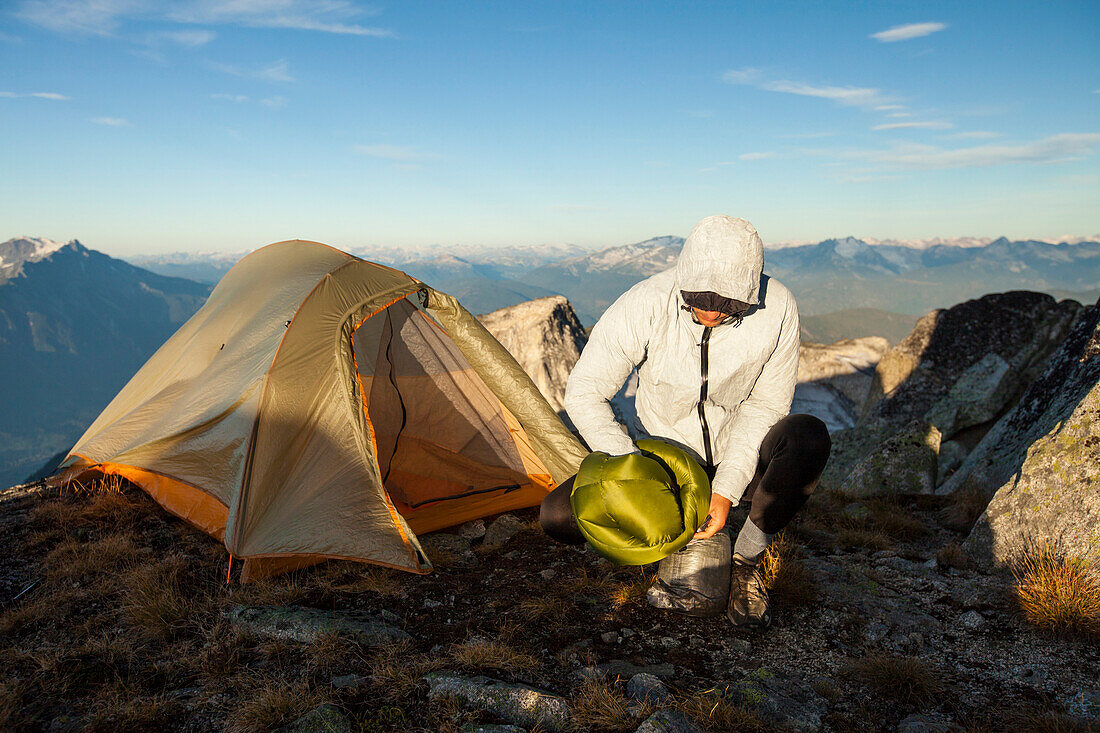An backapcker stuffs his sleeping bag into a stuff sack after camping on  Saxifrage Peak near Pemberton, British Columbia, Canada.
