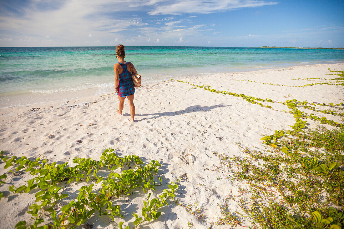 A young woman  walks towards the ocean with her beach bag in Cayo Coco, Cuba.