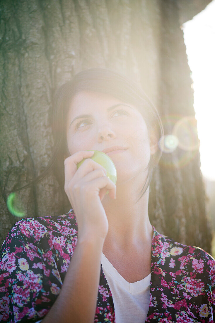 Woman holding apple, looking up dreamily, portrait