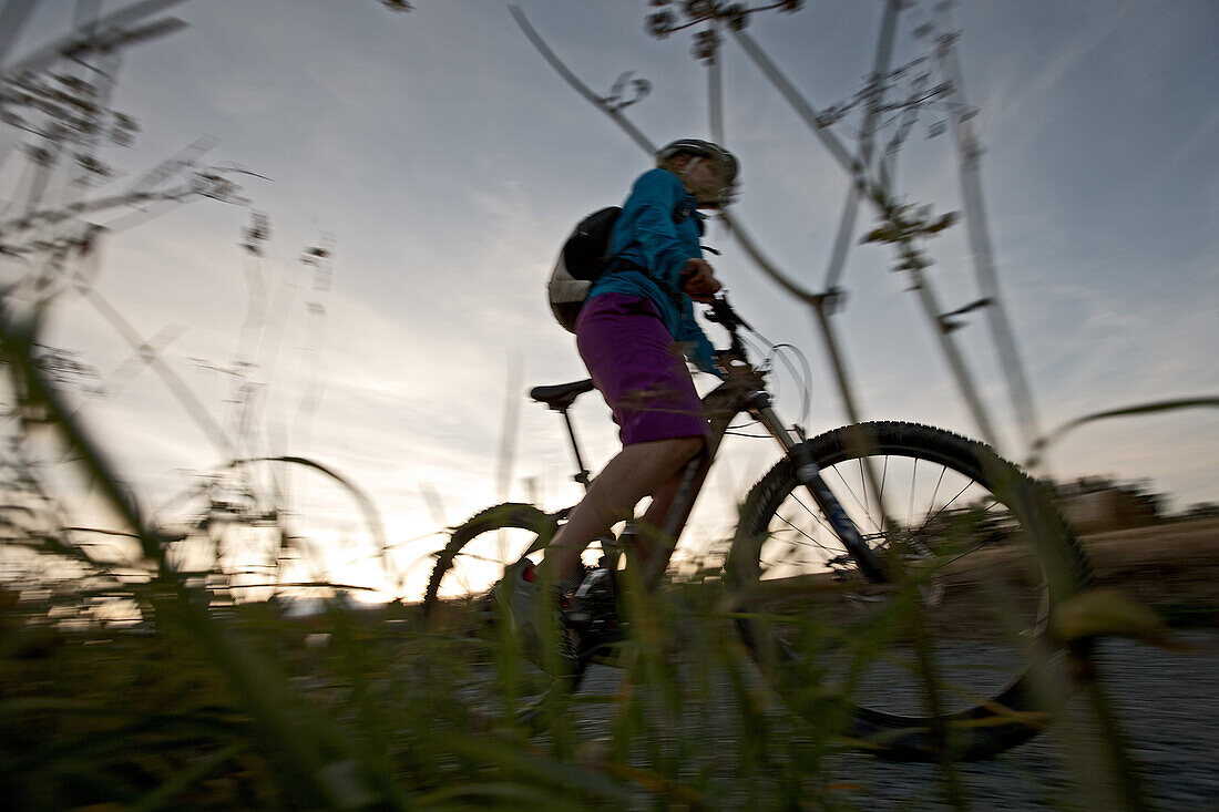 Young woman riding with her bike on a way between fields