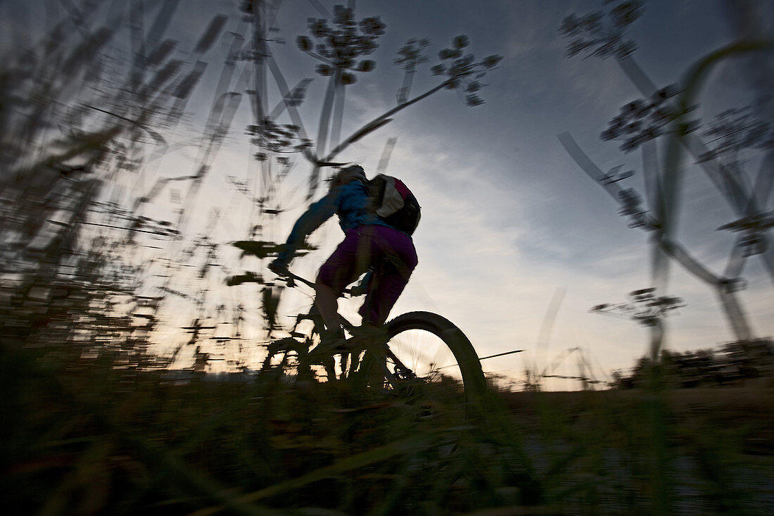 Young woman riding with her bike on a way between fields