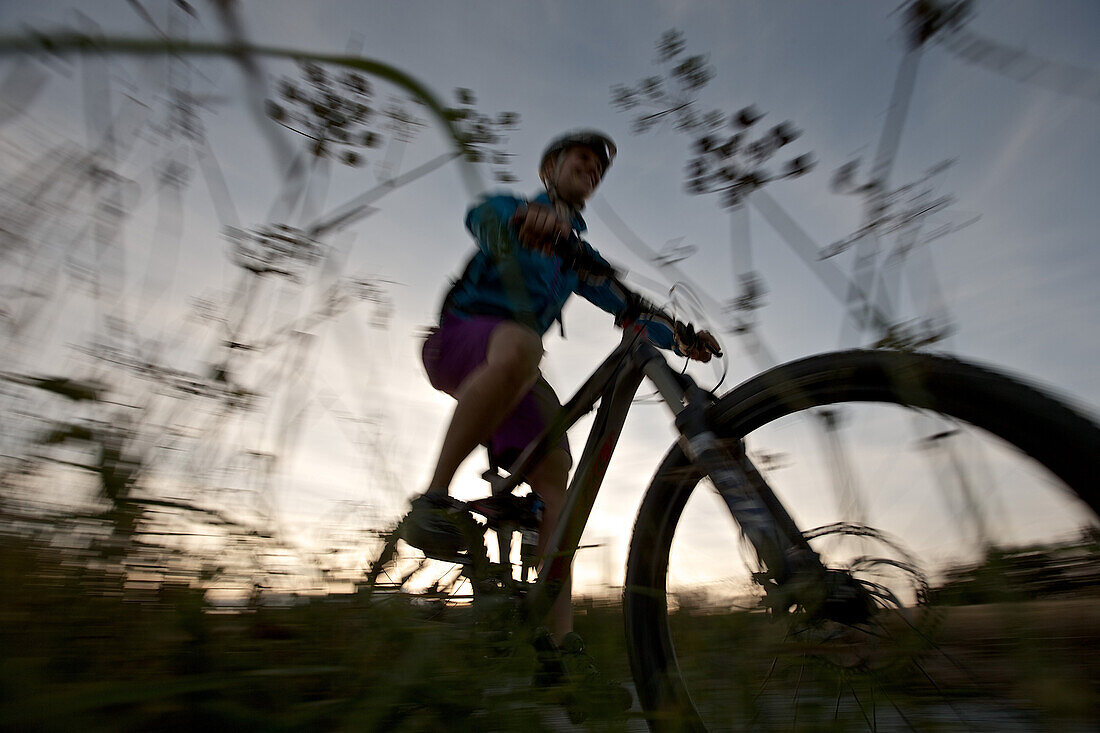 Young woman riding with her bike on a way between fields