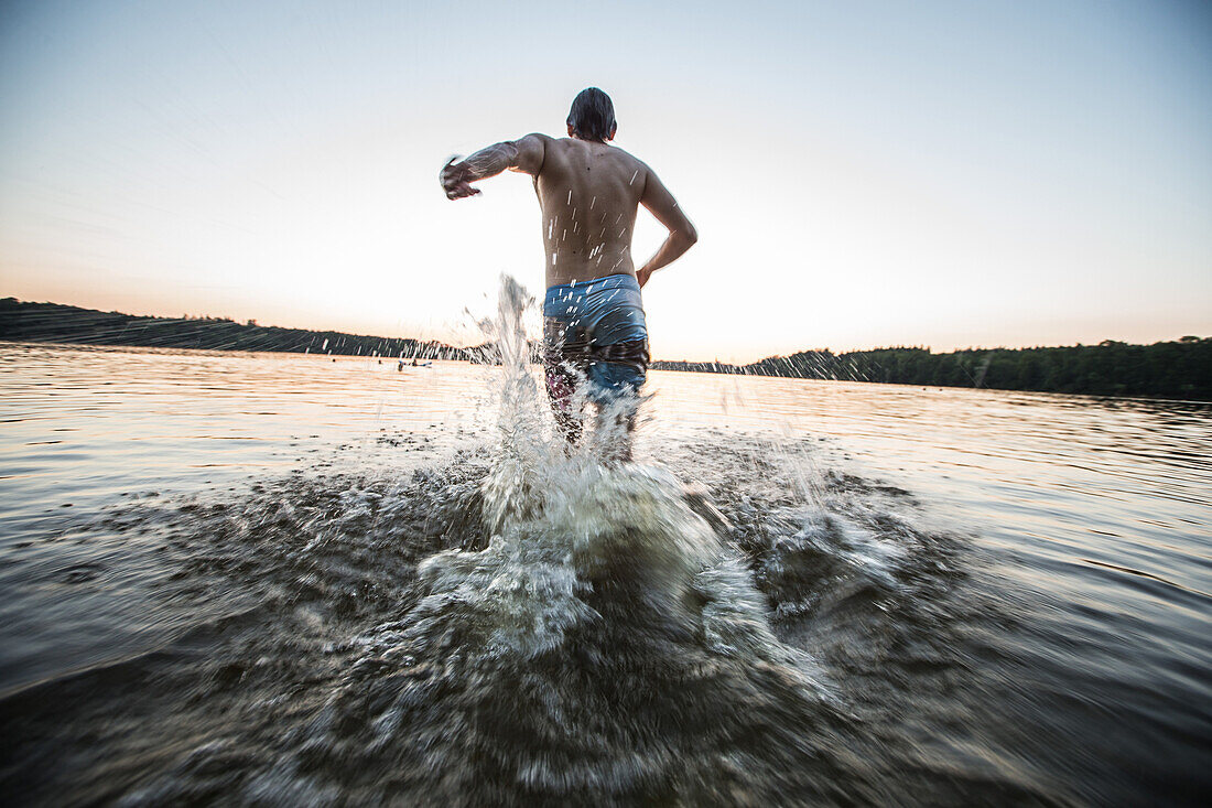 Young man running into the water of a lake, Freilassing, Bavaria, Germany