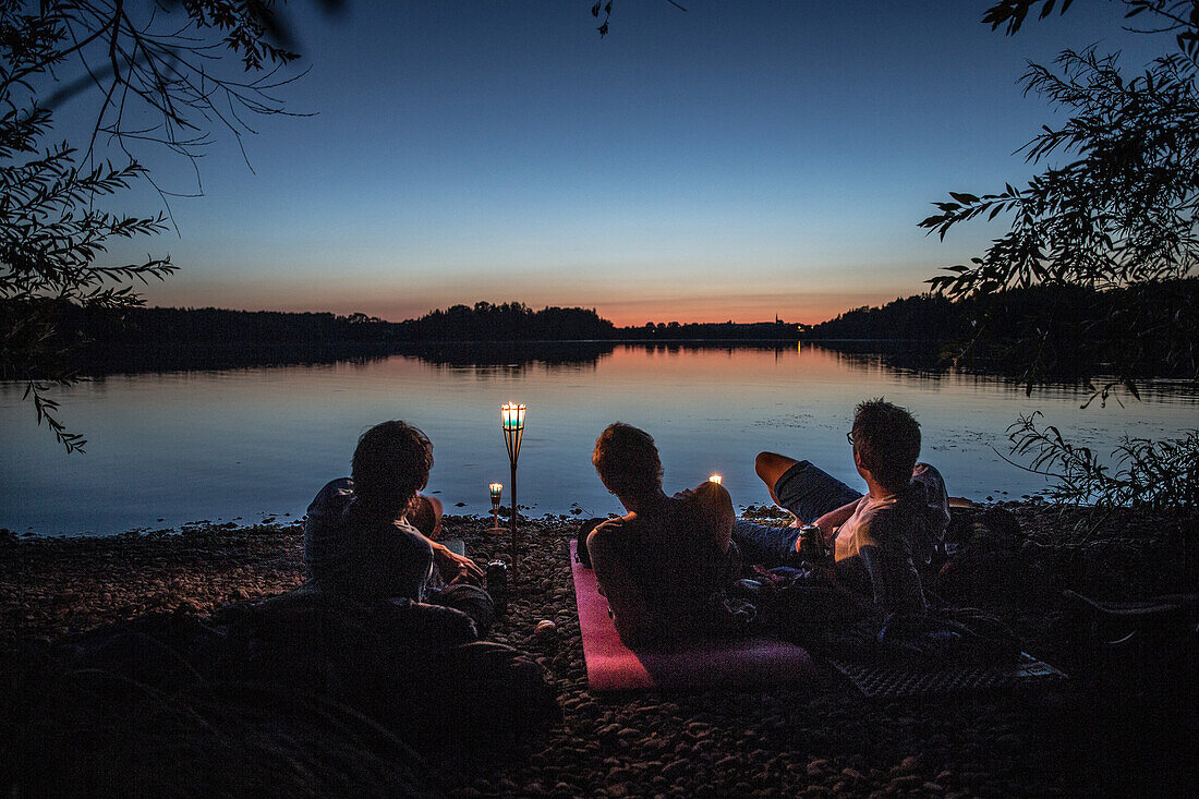 Drei junge Männer liegen an einem See und genießen die Natur, Freilassing, Bayern, Deutschland