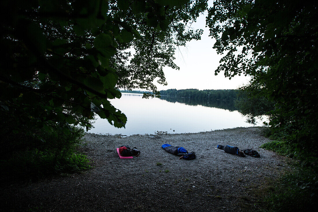 Three young man sleeping outside only with sleeping bags at a lake, Freilassing, Bavaria, Germany