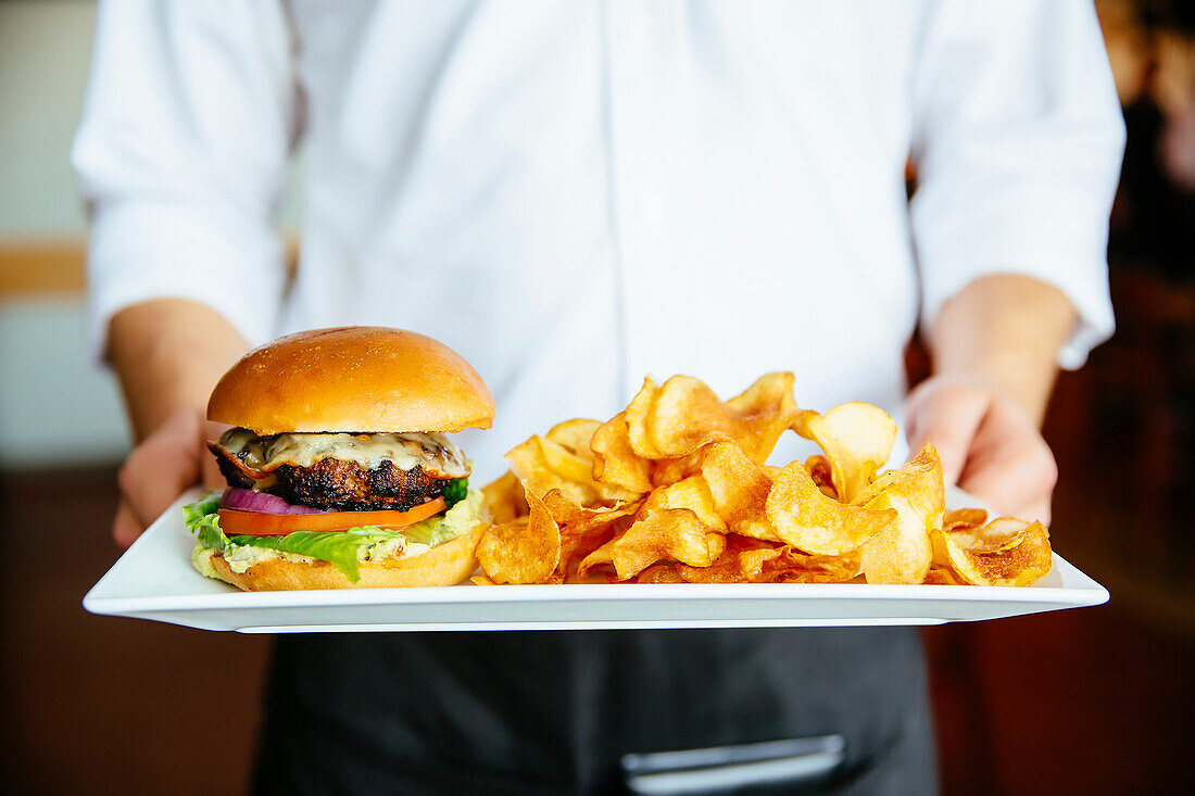 Caucasian waiter holding plate of cheeseburger and chips