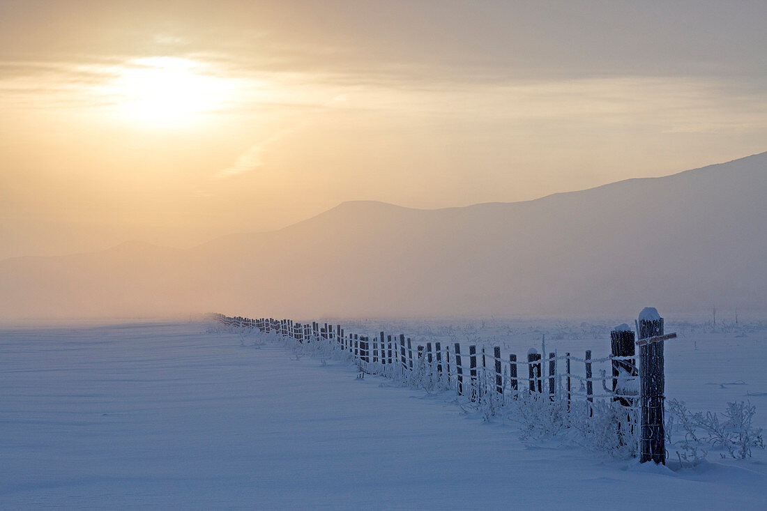 Sunrise over fence in snowy rural landscape