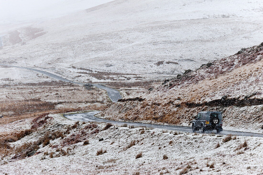 A four wheel drive vehicle negotiates a road through a wintry landscape in the Elan Valley area in Powys, Wales, United Kingdom, Europe