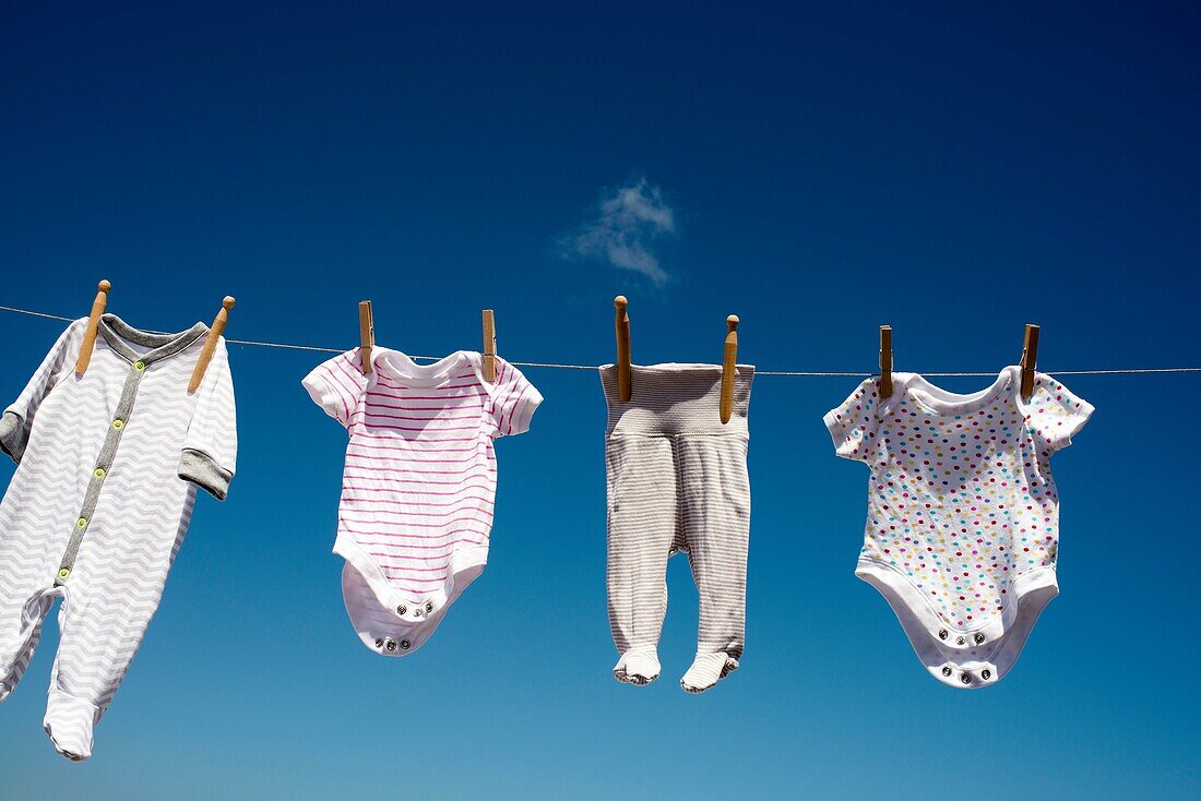Baby clothes hanging in the sun with blue sky in the background.