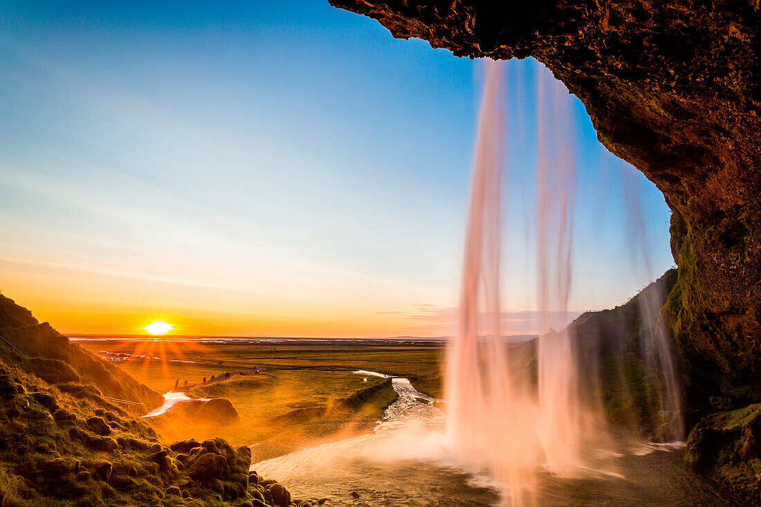 Iceland landscape, Seljalandsfoss waterfall at sunset, picture taken from behind the fall with sunburst