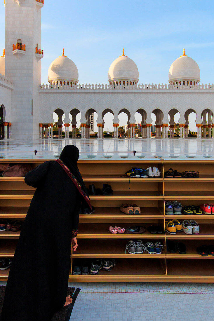 Abu Dhabi, United Arab Emirates. Woman taking off her shoes before entering the Sheikh Zayed Grand Mosque