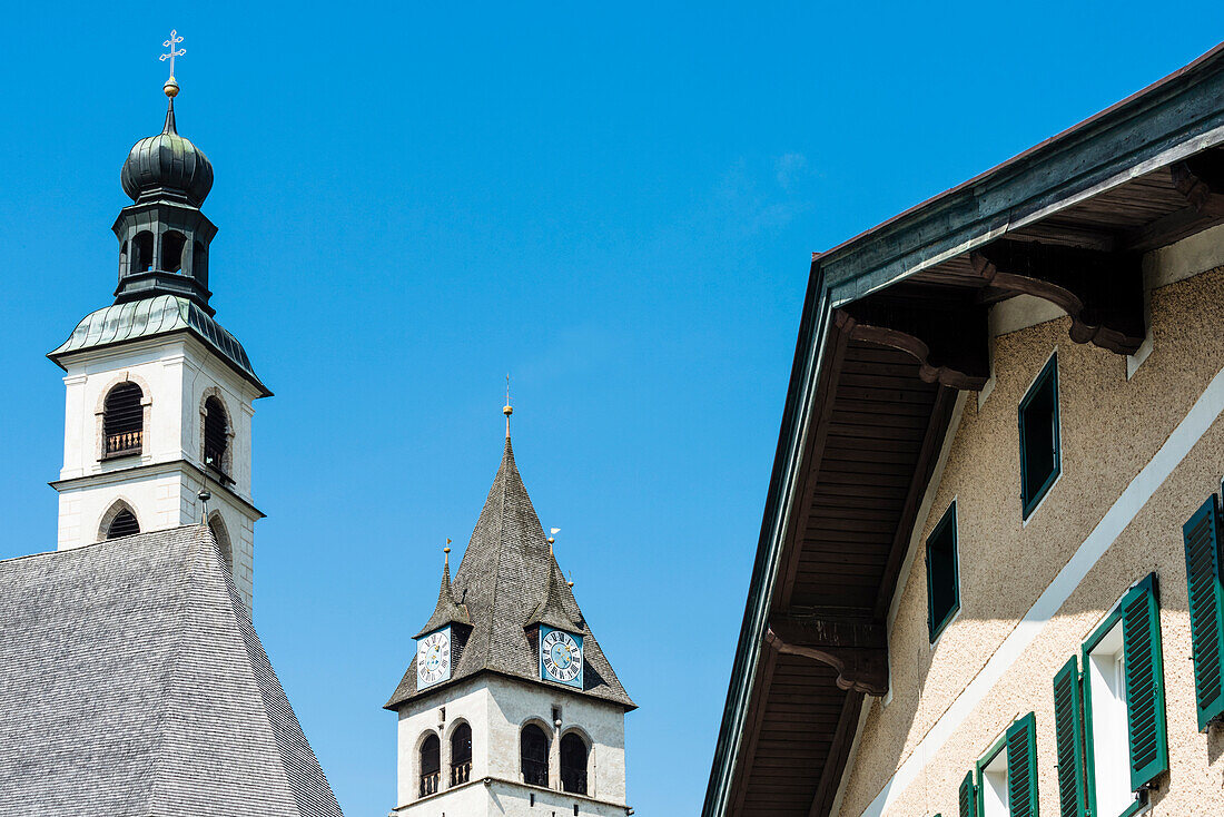 The towers of the parish church Saint Andreas and in the background of the church Liebfrauenkirche and a town house with window shutters in the Old Town, Kitzbühel, Tyrol, Austria