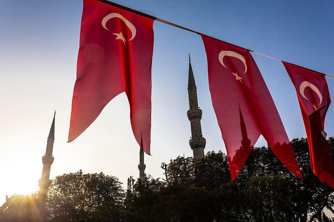 Die Minarette der Blauen Moschee, Sultan-Ahmed-Moschee, im Morgenlicht zwischen den Nationalflaggen die über dem Hippodrom hängen, Istanbul, Türkei