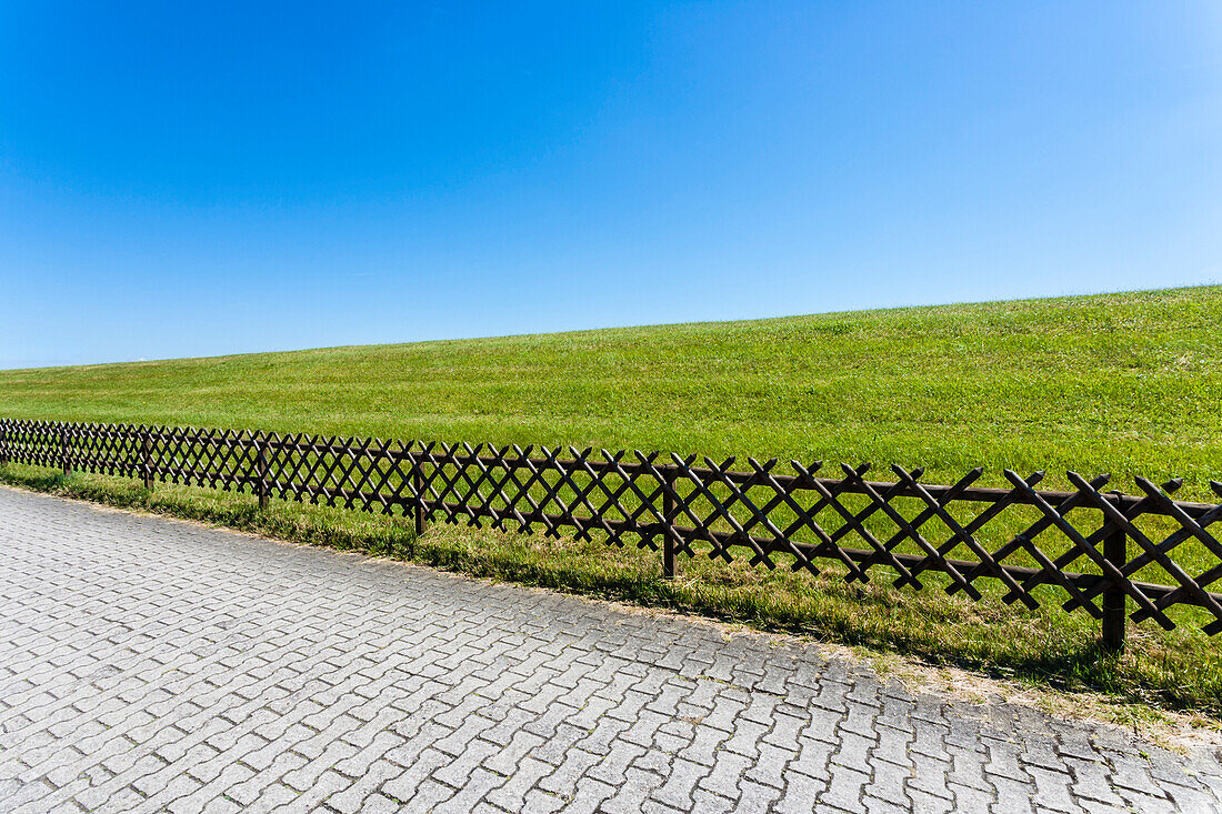 A typical German wooden lattice fence seperates the way with interlocking pavement from the dyke, Juist, Schleswig Holstein, Germany