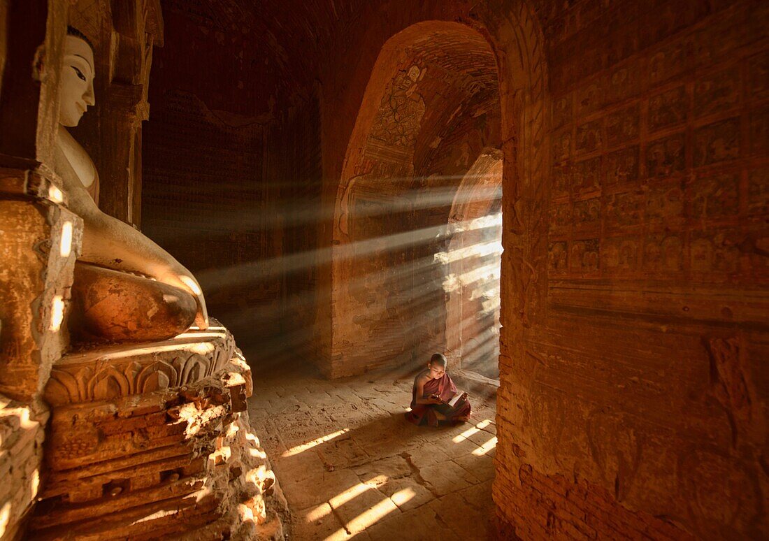 A young monk reading with rays of sunlight in the temples of Bagan, Myanmar.