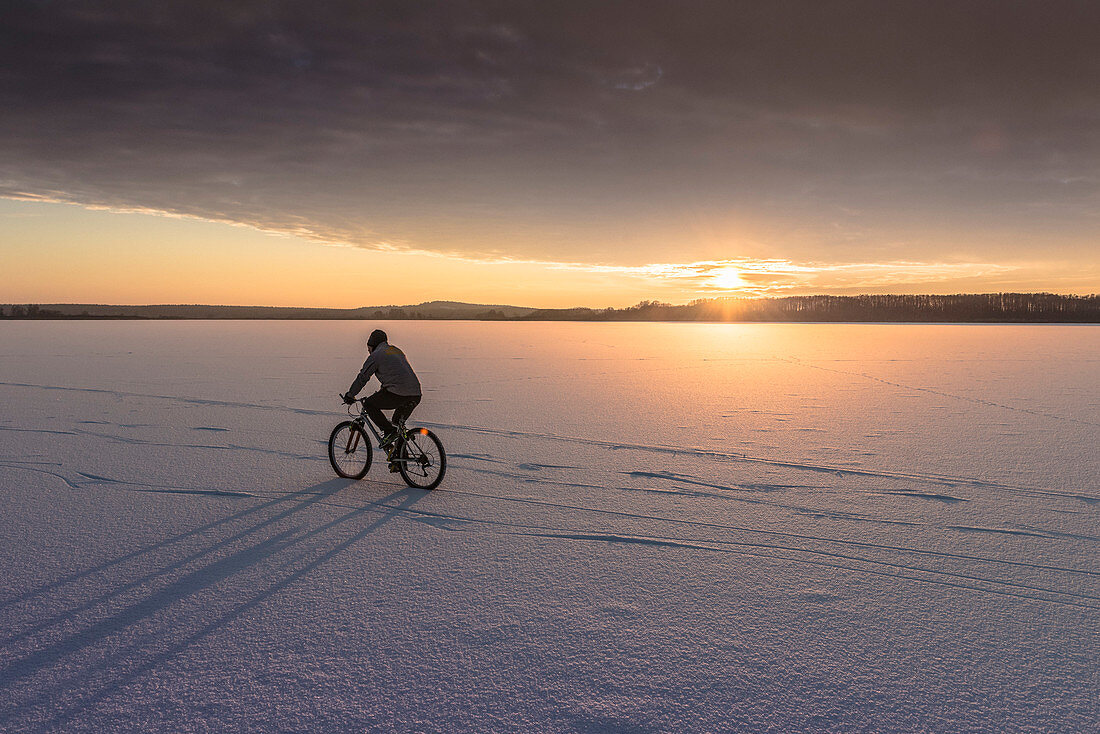 Einsamer Radfahrer zieht die ersten Bahnen auf dem zugefrorenen Rangsdorfer See bei Sonnenuntergang - Deutschland, Brandenburg, Rangsdorf