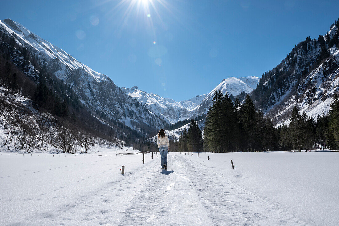 Frau spaziert im Winter bei Sonne, blauem Himmel und Schnee durch das Bergpanorama des Stillachtals - Deutschland Oberallgäu Oberstdorf