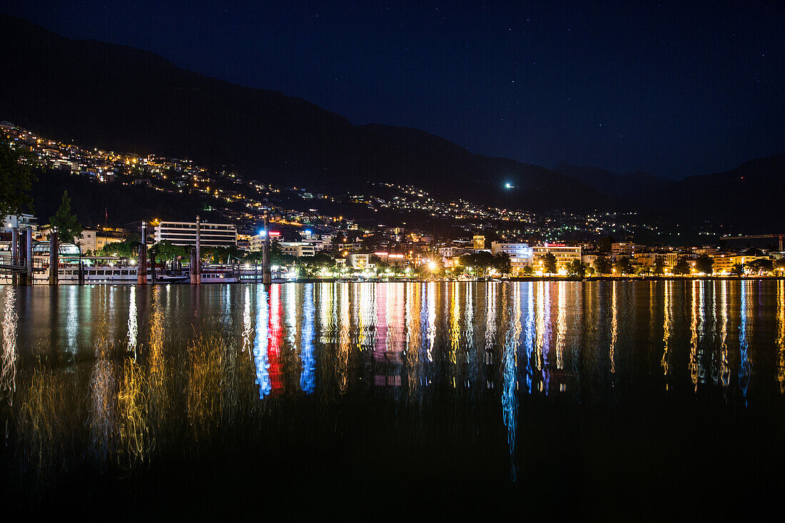 Reflektierende Lichter einer Stadt in einem See bei Nacht, Lago Maggiore, Tessin, Schweiz
