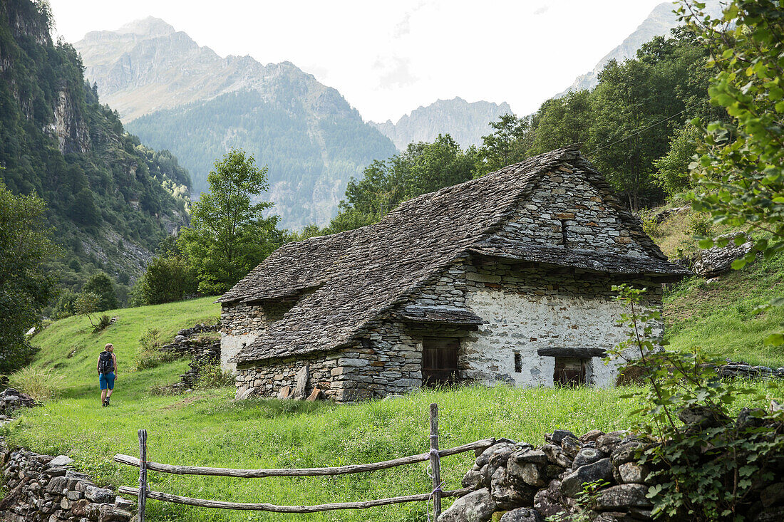 Young female hiker walking past an old house in the mountains, Valle Verzasca, Ticino, Switzerland
