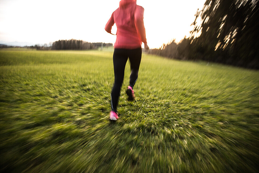 Young woman running over a field, Allgaeu, Bavaria, Germany